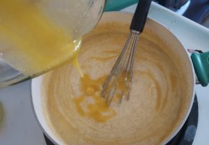 Adding eggs to the creamy wheat pudding